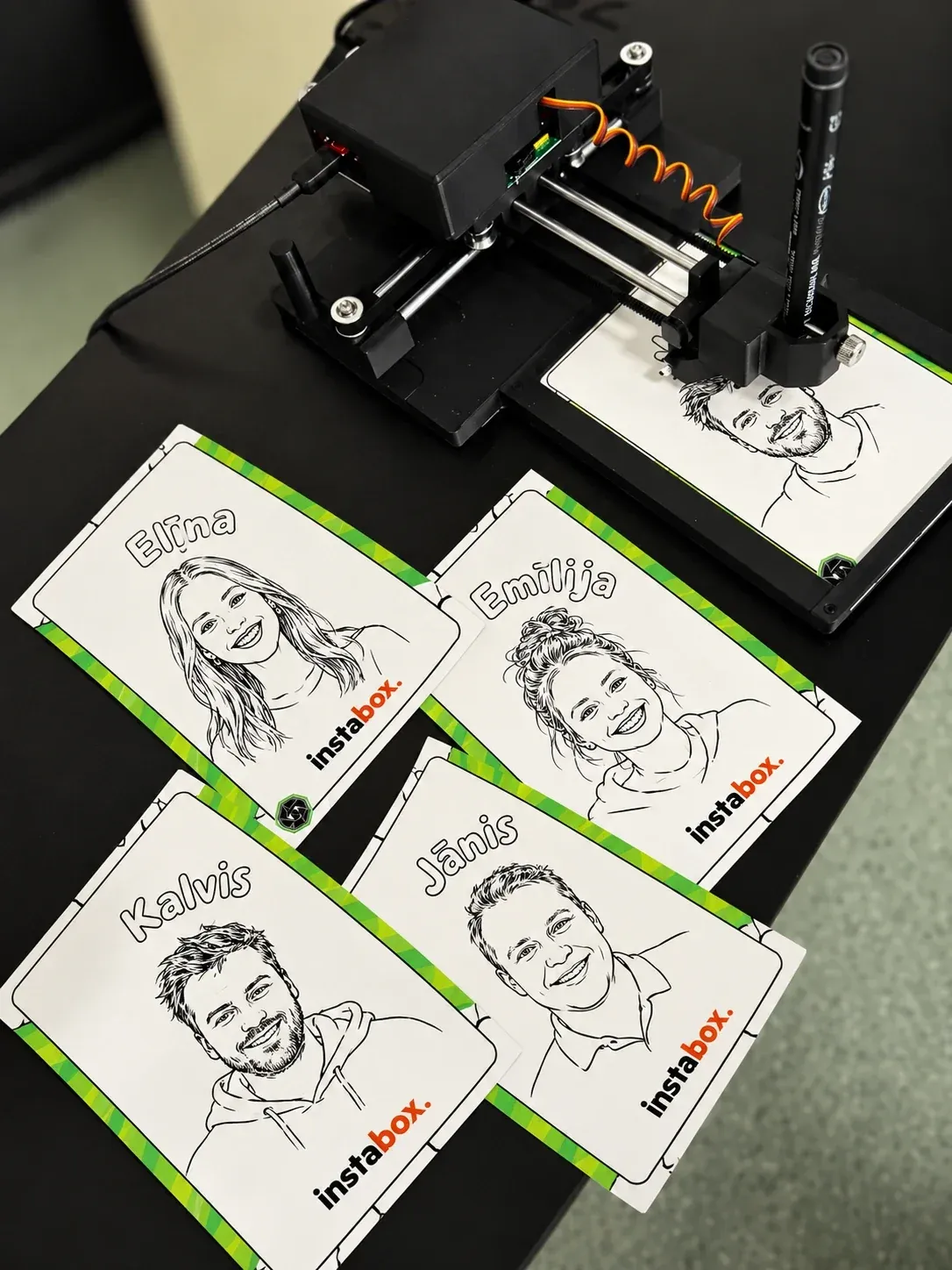 AI karikatūru robots zīmē portretu, blakus gatavas viesu karikatūras ar Instabox logo