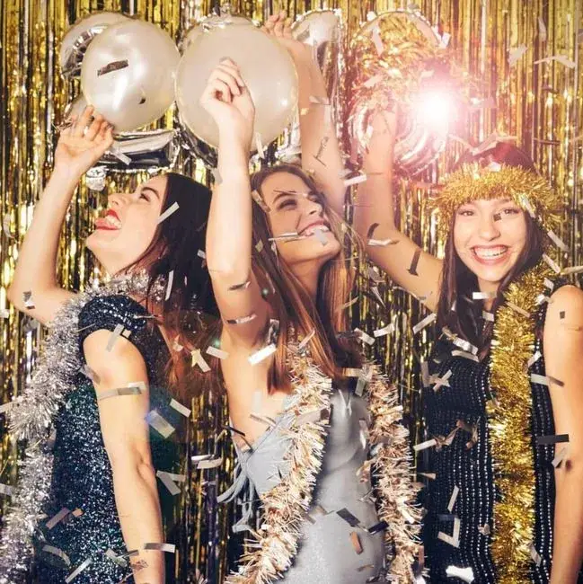 Viesas ar konfeti un zelta virtenēm pozē foto kastē ziemas ballītē